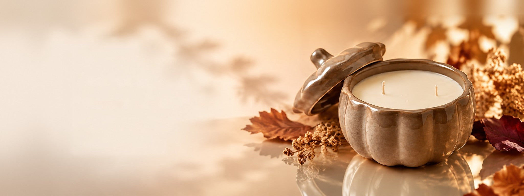Bougie citrouille en céramique ouverte, son couvercle posé à côté, entourée de feuilles d’automne