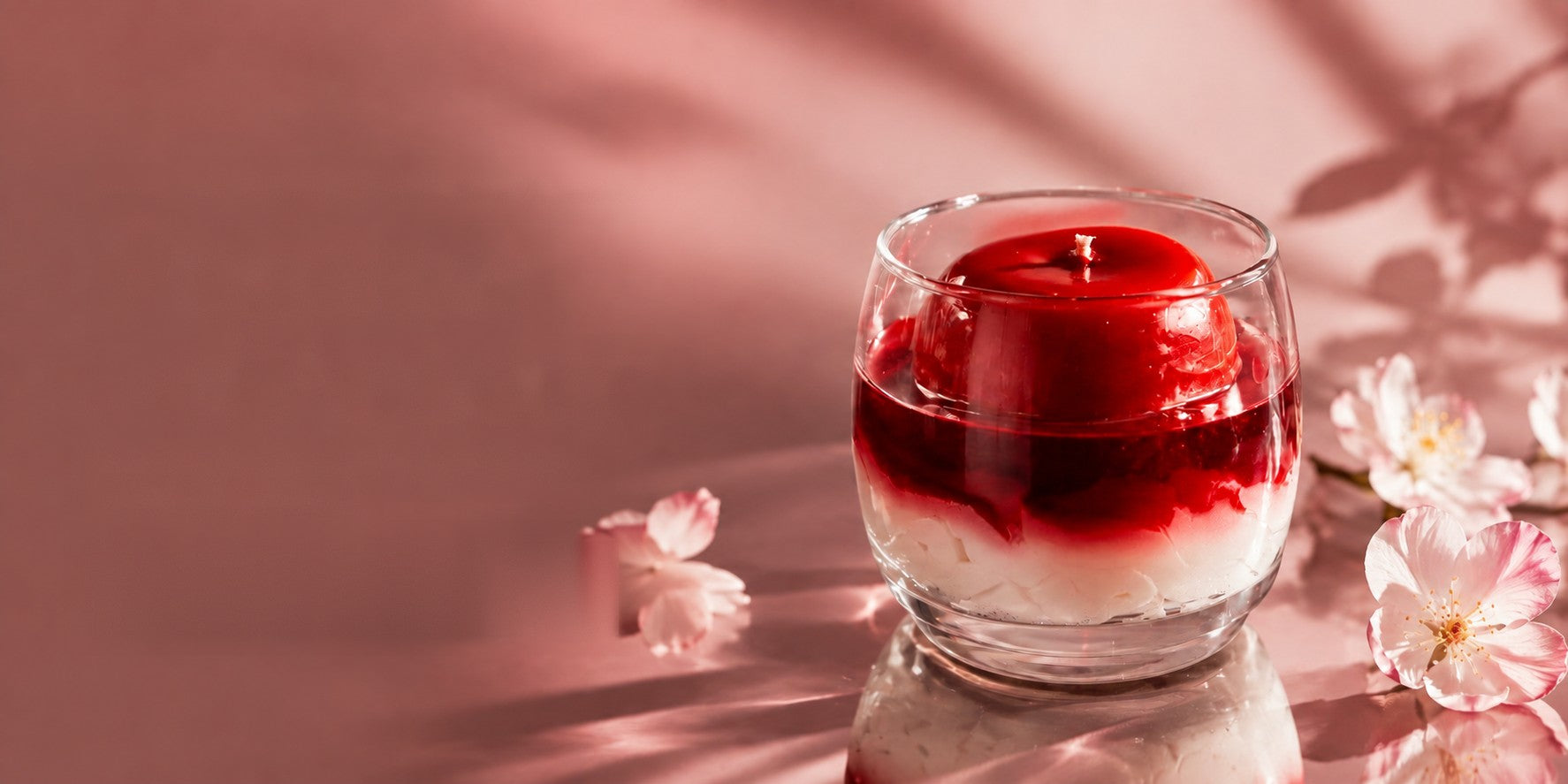 Bougie Pomme d’amour Ajouba dans son verre, sur fond rosé fleuri